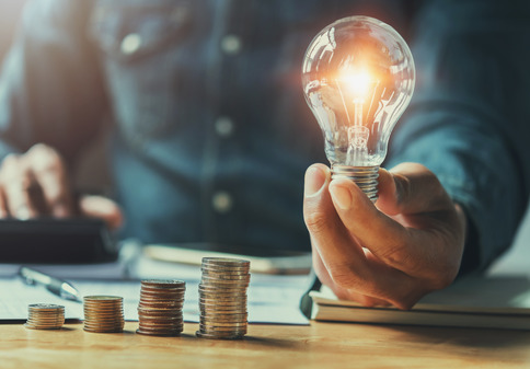 Business man holding light bulb on the desk in office and calculating on calculator